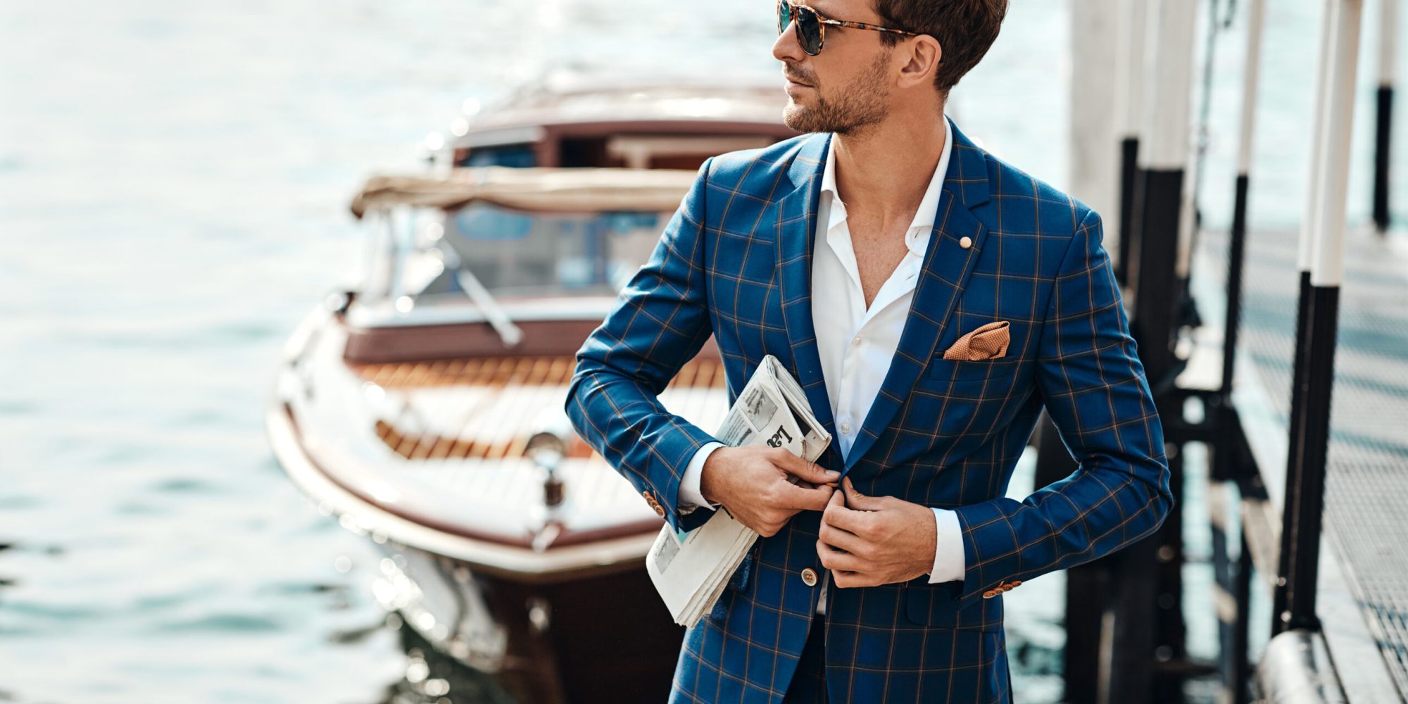 Young handsome man in classic suit over the blurred lake buttoning his jacket